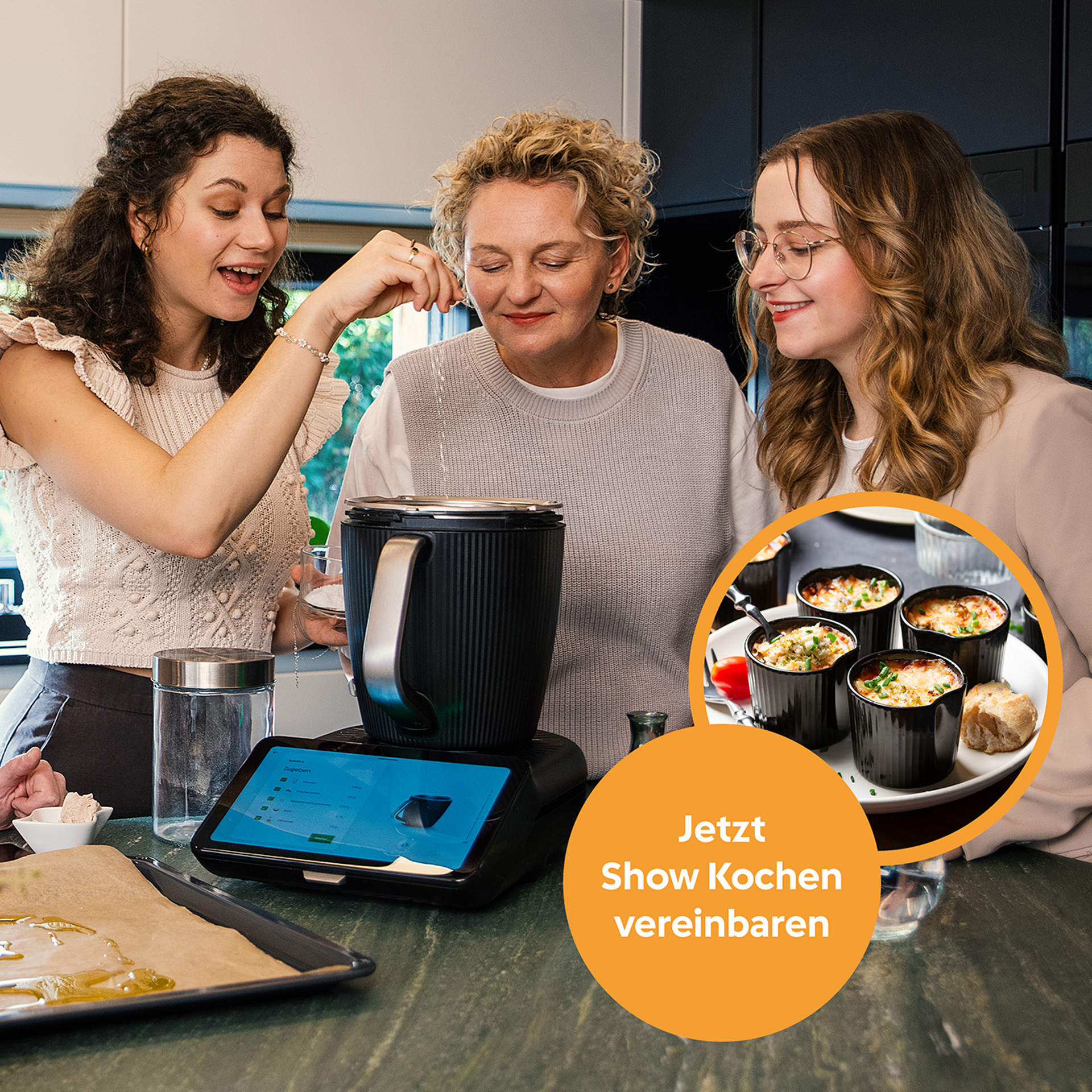 Drei Personen bereiten mit Thermomix® TM7 und Kochbechern in einer Küche Speisen zu, Werbung für Show Kochen.