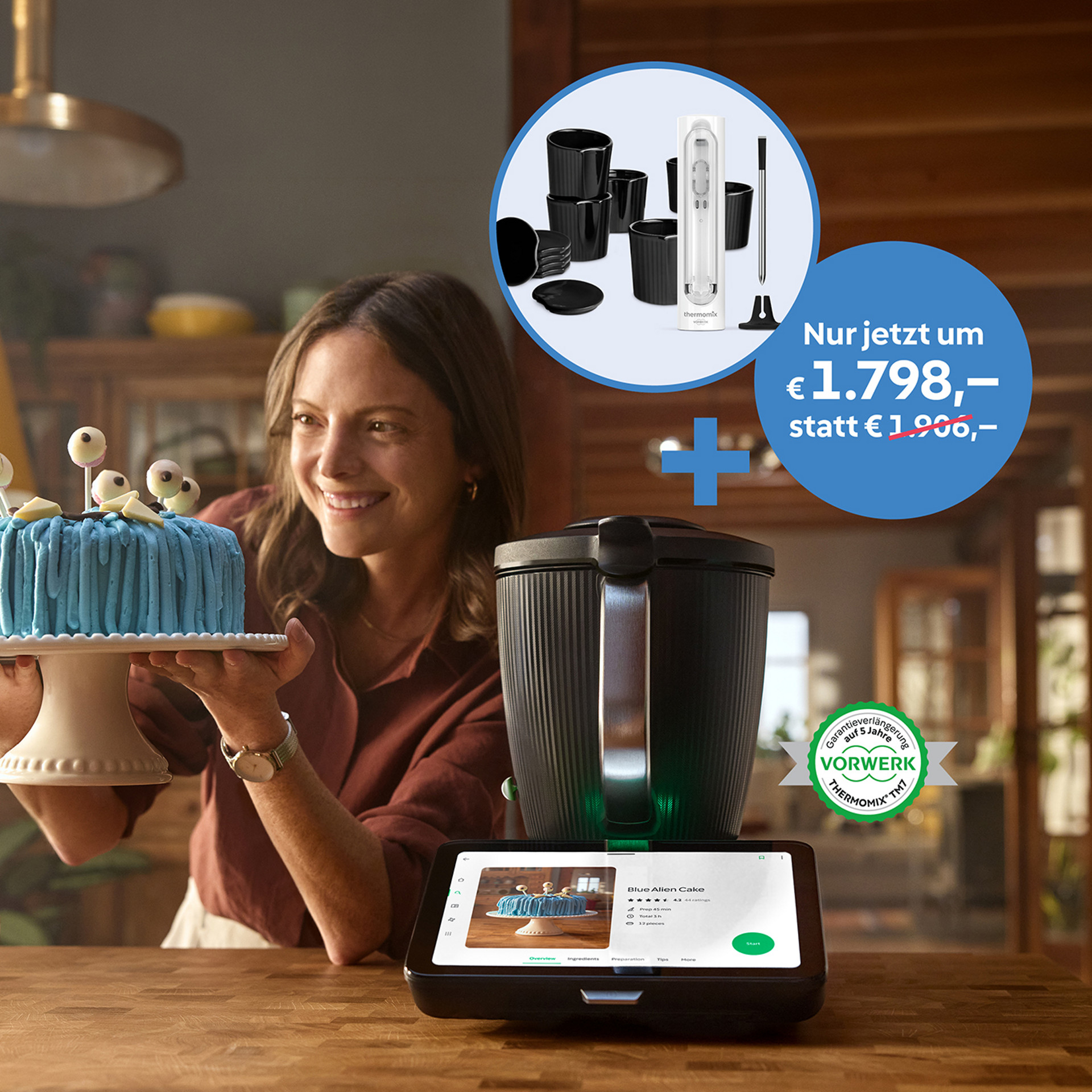 Frau präsentiert eine blaue Torte neben einem Thermomix® TM7, Zubehör und Aktionspreis sind abgebildet.