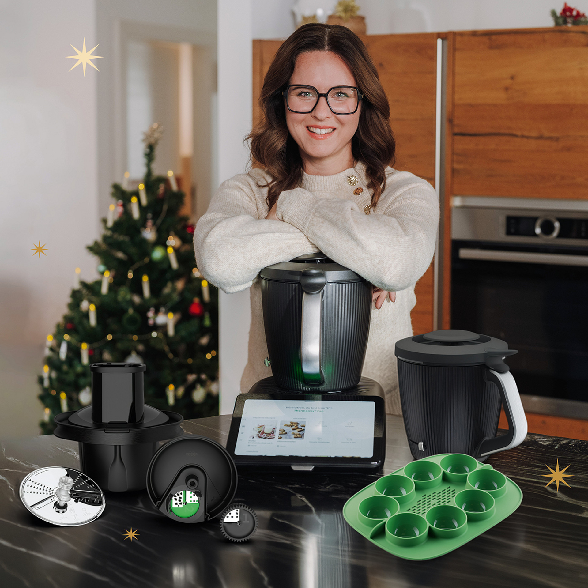 Frau in einer Küche mit Weihnachtsbaum, Thermomix® TM7, Thermomix® TM7 Gemüse Styler Plus und Zubehör auf der Arbeitsplatte.