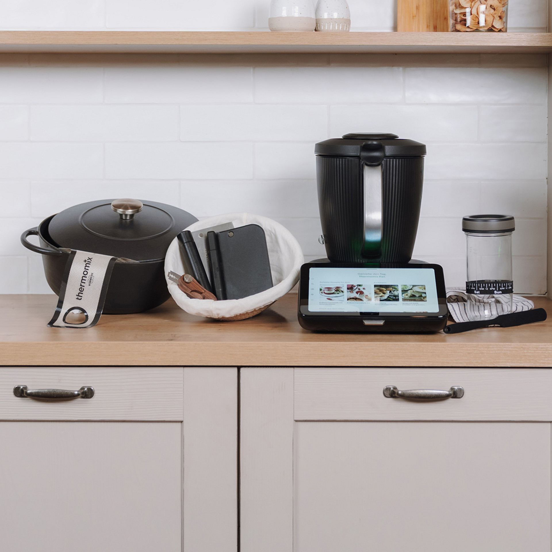 Thermomix® TM7 auf einer Küchenarbeitsplatte neben einem Gusseisen-Topf, Notizbüchern, Glasbehälter und Messbecher.