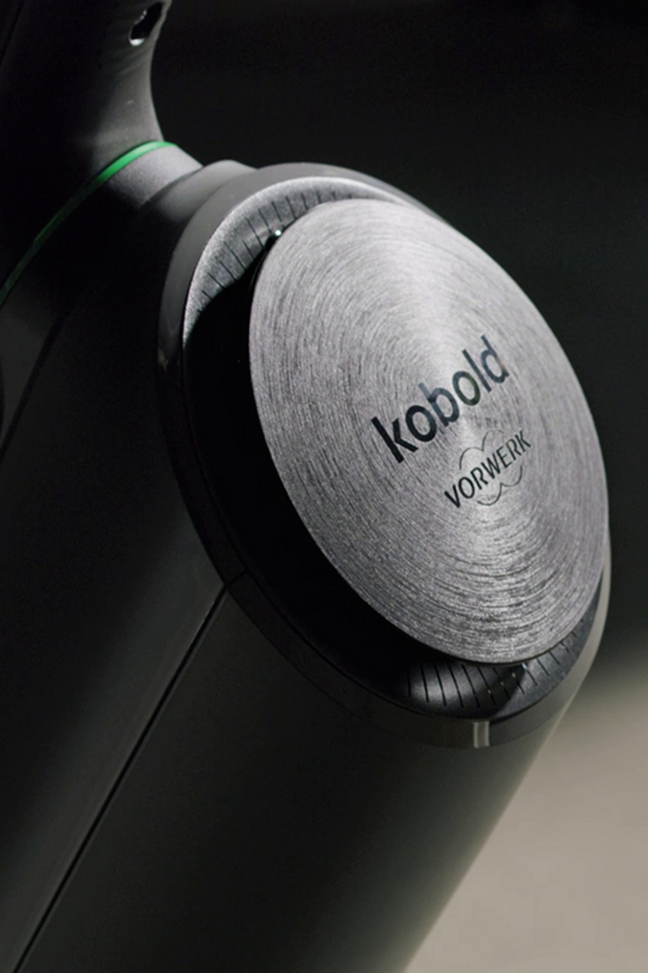 Primer plano del detalle metálico del logotipo en un Kobold VK7 de Vorwerk, mostrando el acabado cepillado.