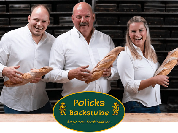 Zwei Männer und eine Frau mit Baguette in einer Backstube