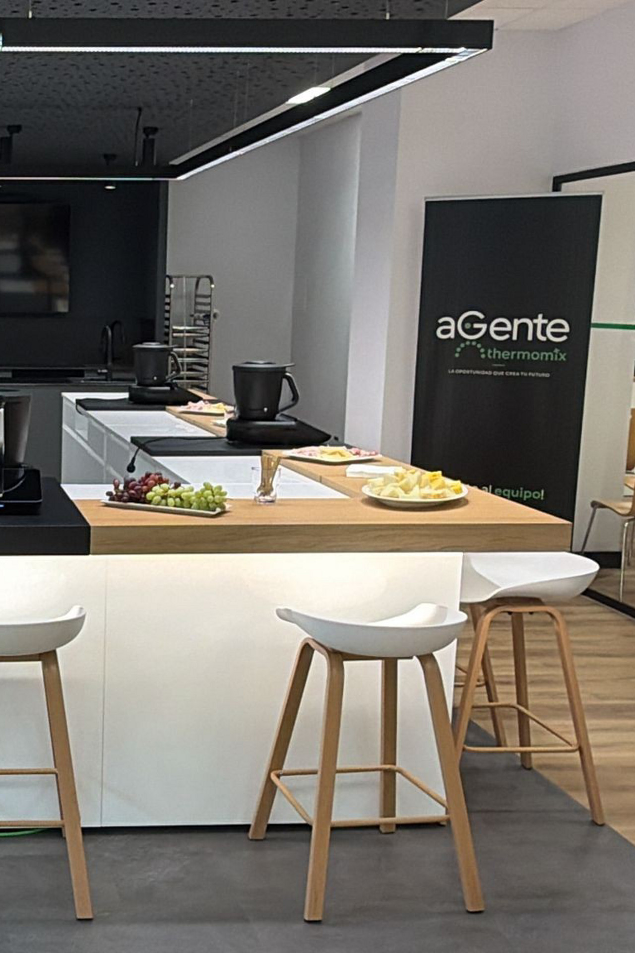 Estudio de cocina moderno con cinco Thermomix® TM6 en encimeras, rodeados de taburetes y platos de fruta.
