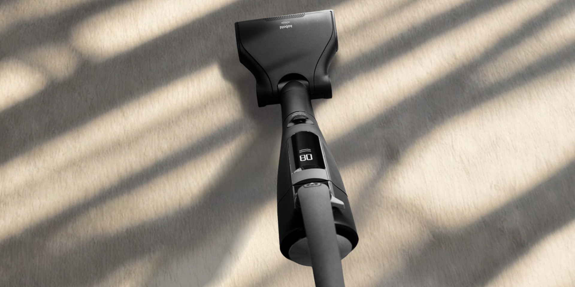 Pessoa usando Kobold VK7 Black Edition com a EB7, sobre piso claro, vista superior, sob sombras de luz solar.