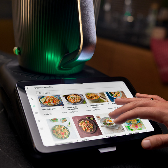 Hand interacting with the touchscreen of a Thermomix TM7 displaying recipe search results on a kitchen counter