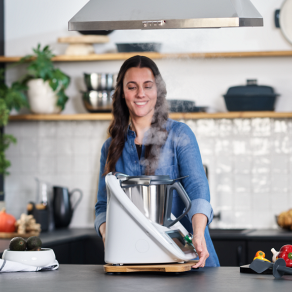 Pessoa na cozinha usando Bimby TM6 com vapor saindo do aparelho