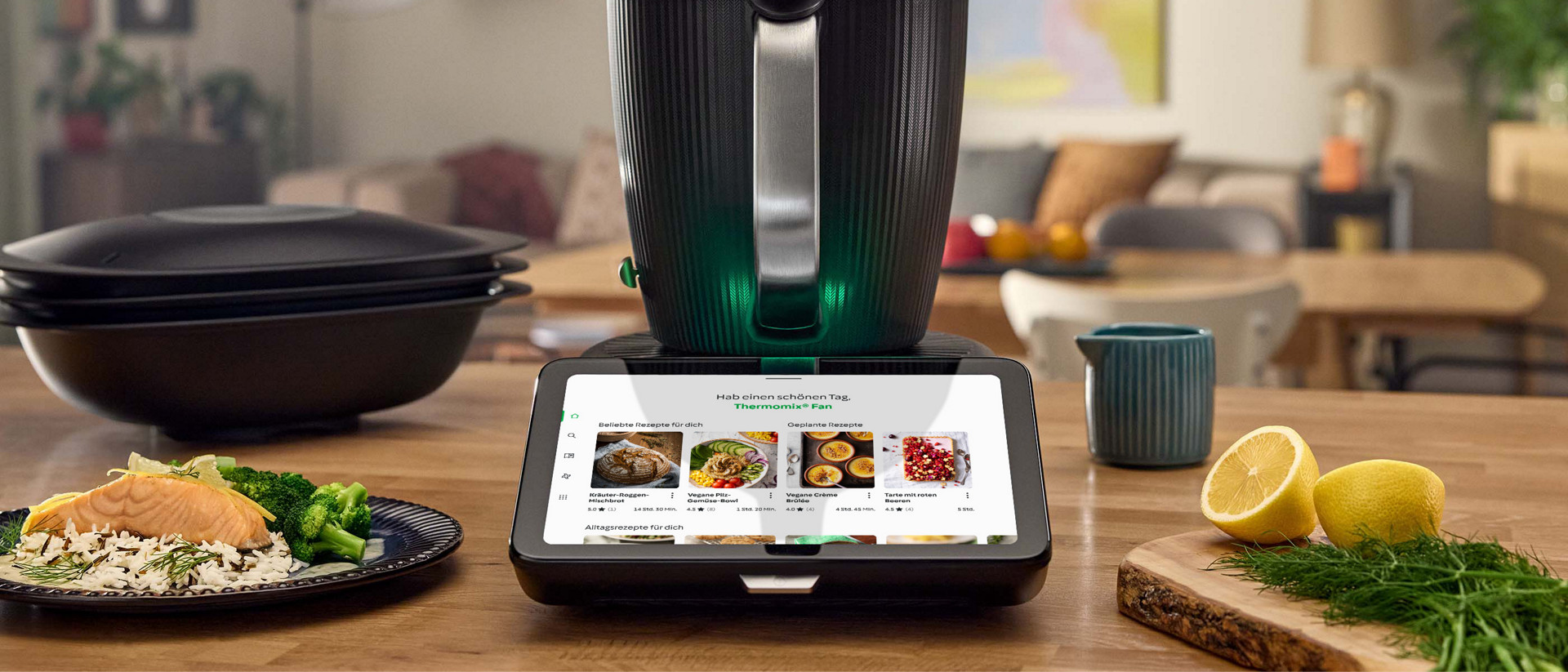 Thermomix® TM7 auf der Küchenarbeitsplatte mit Rezeptanzeige, umgeben von Lebensmitteln, Zitronen und Schalen.