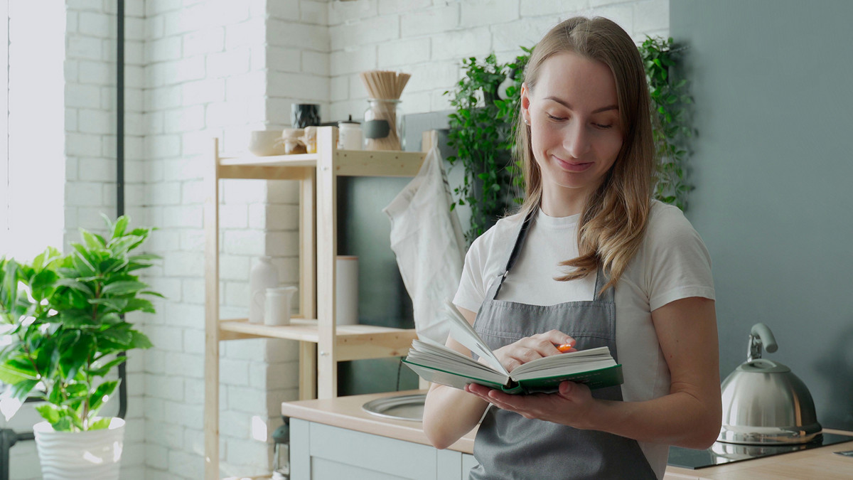 Young woman reading cookbook in the kitchen, looking for recipe.