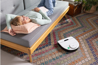 Femme sur un canapé avec robot aspirateur au sol