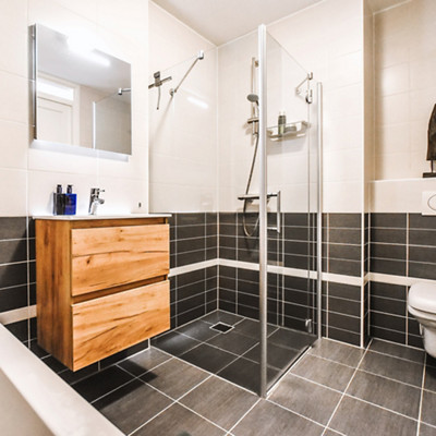 Salle de bain au carrelage gris avec une douche aux parois en verre et une baignoire