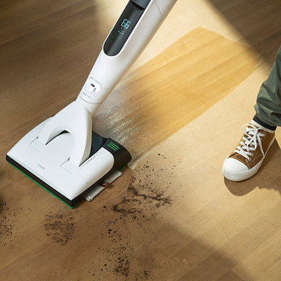 Un homme passe l'aspirateur laveur VK7 de chez Kobold sur son parquet avec de la terre.