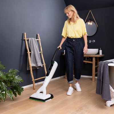 Une femme passe l'aspirateur laveur VK7 Kobold sur son parquet dans sa salle de bain