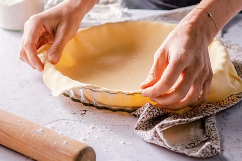 Photo d'une femme étalant une pâte brisée dans un plat à tarte