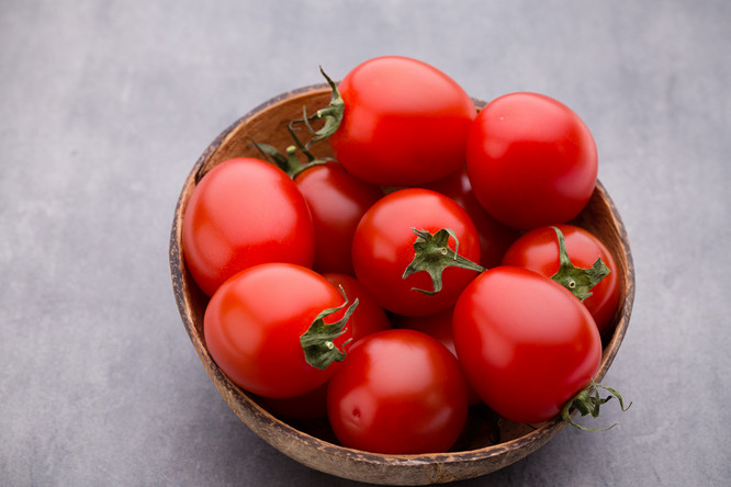 Cherry tomatoes. Three cherry tomatoes in a wooden bowl on a gray background.