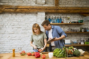 Trendy couple peeling and cutting fresh vegetables from the market in rustic kitchen