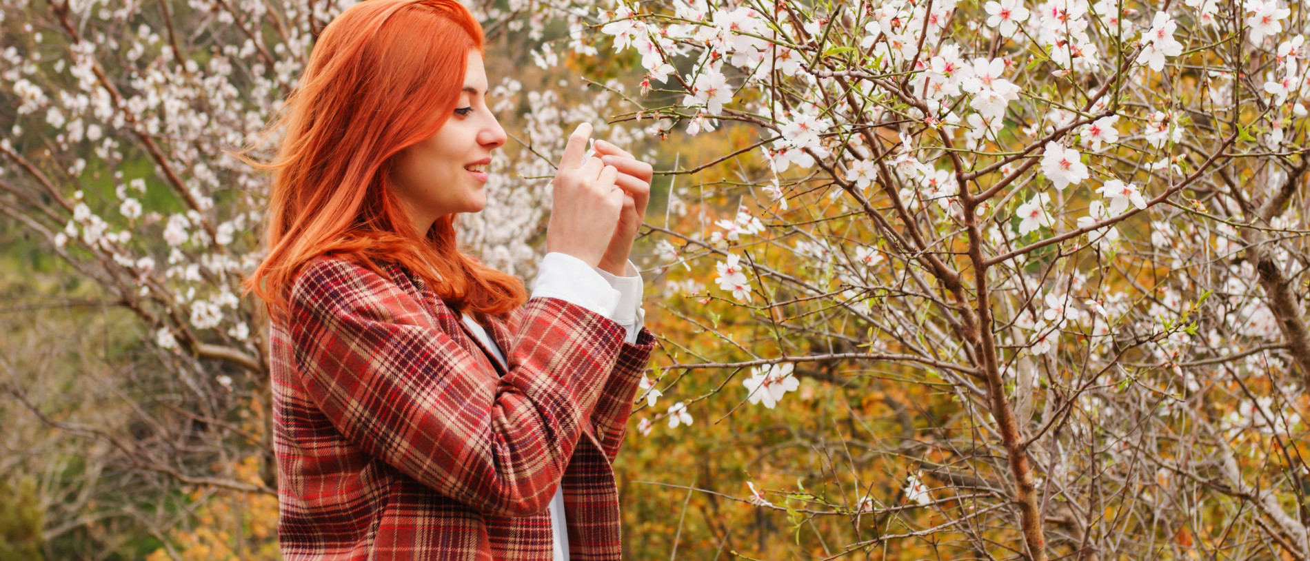 happy red-haired girl under spring flower tree