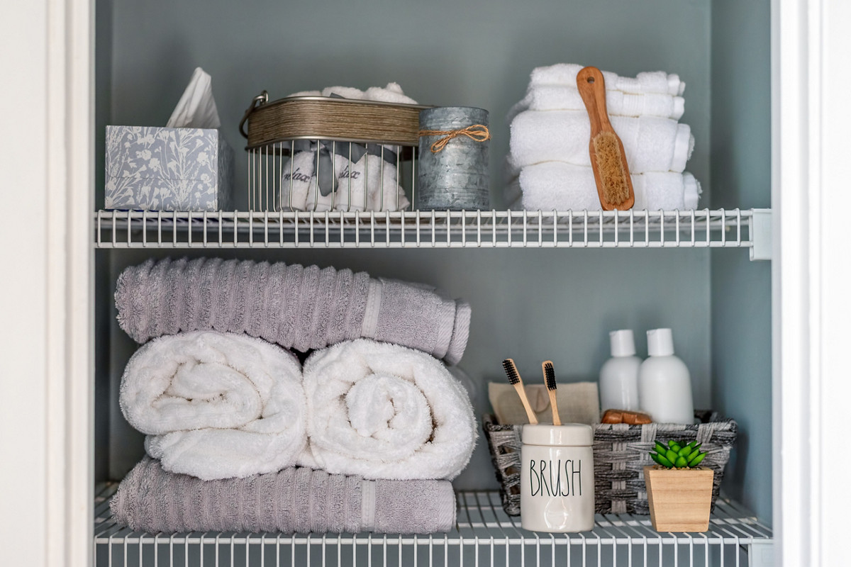 Neatly organized bathroom linen closet with bamboo toothbrushes and white towels