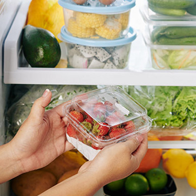 Hands of housewife putting package of strawberries in refrigerator full of groceries she ordered online