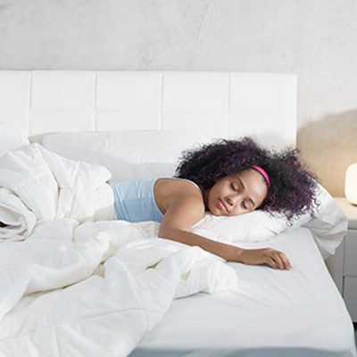 Young African American woman waking up at home. Portrait of happy black girl smiling, enjoying a large king size mattress all for herself.