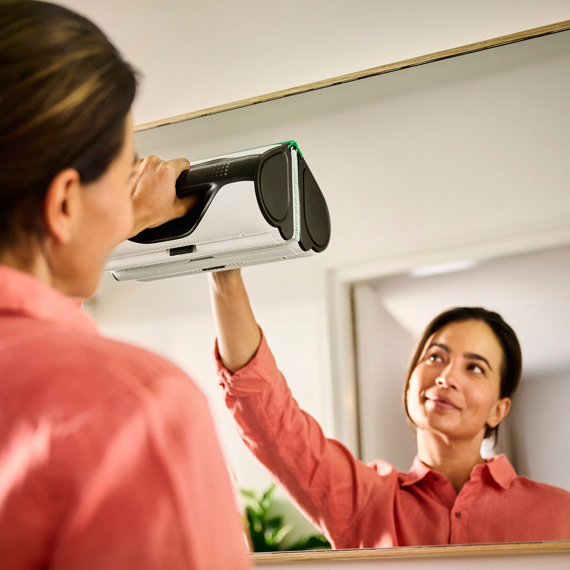 Eine Person reinigt einen Spiegel mit dem Kobold VG100+ Flächenreiniger in einer modernen Wohnung.