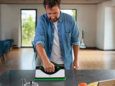 Frau saugt mit Kobold VK7 einen Hartboden im Haus-Eingangsbereich, während ein Mann sein Fahrrad zur Tür reinschiebt
