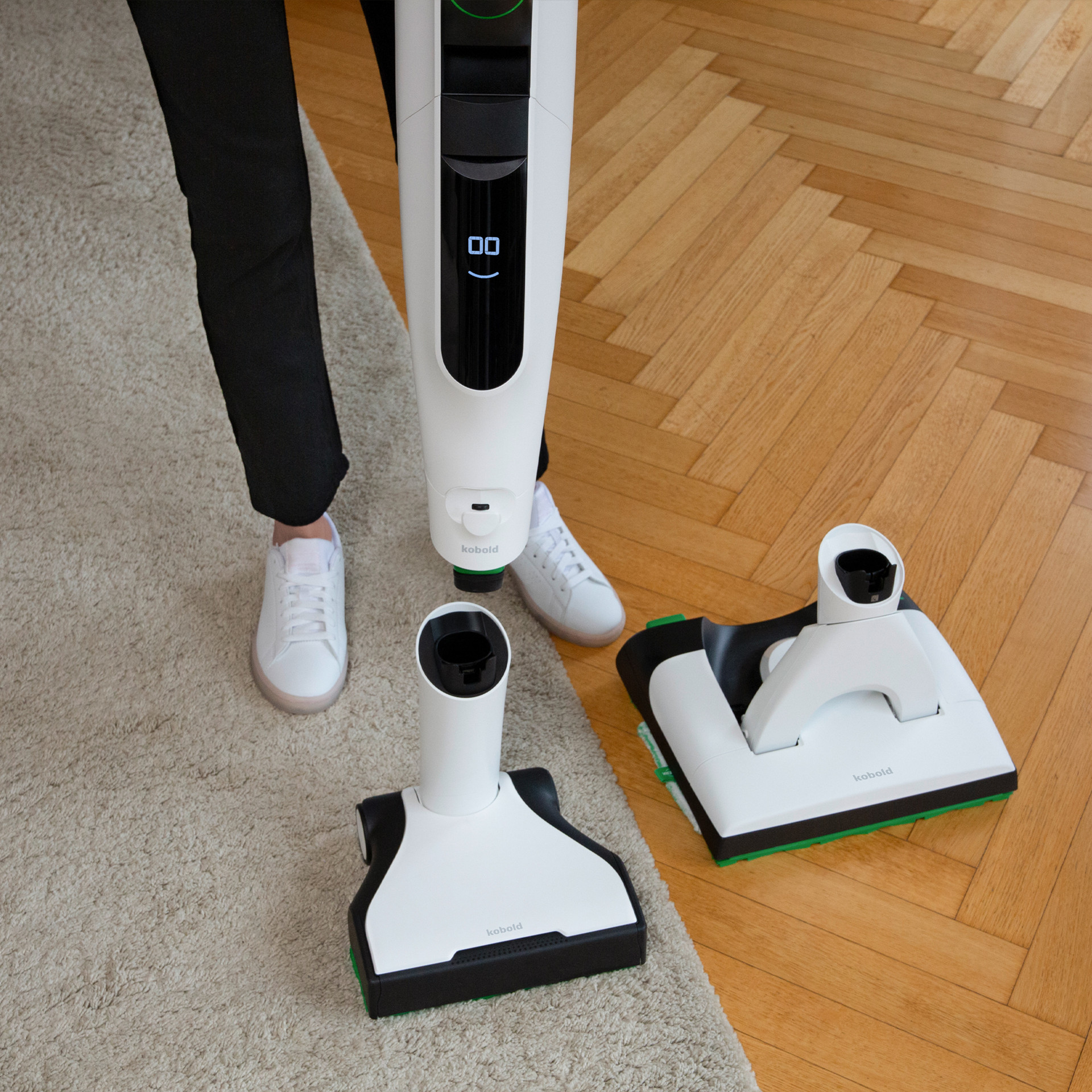 Person using Kobold VK7 on carpet with EB7 and SP7 attachments placed on a wooden floor nearby.
