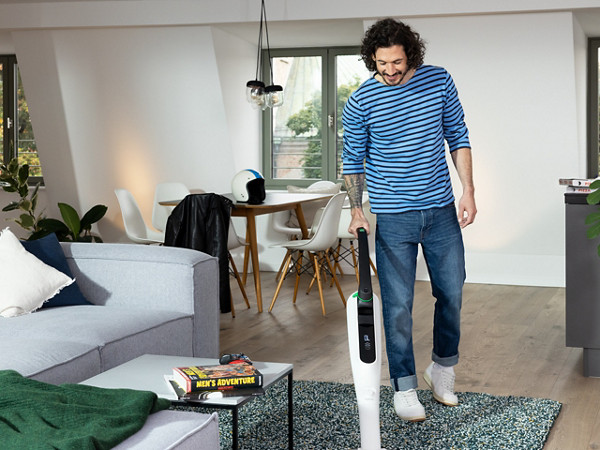 Ein Mann reinigt seinen Wohnzimmerteppich mit dem K7 Akku-Staubsauger