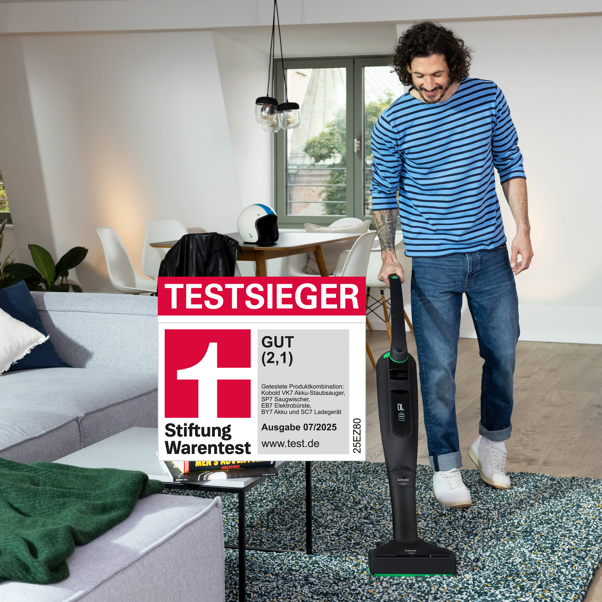 Mann saugt Wohnzimmerteppich mit Kobold VK7. Stiftung Warentest Testsieger-Siegel im Vordergrund sichtbar.