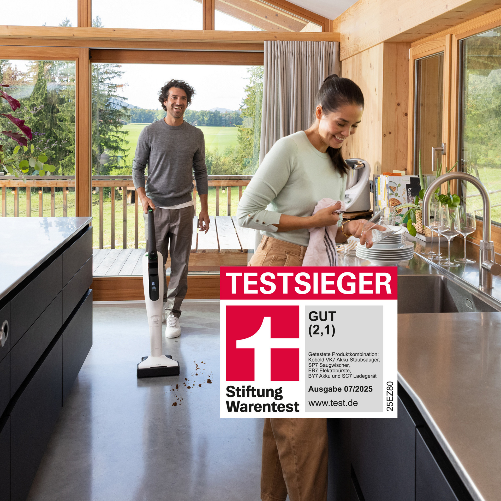 Mann nutzt Kobold VK7 Akku-Staubsauger in heller Küche, Frau am Spülbecken, Stiftung Warentest Auszeichnung im Vordergrund.