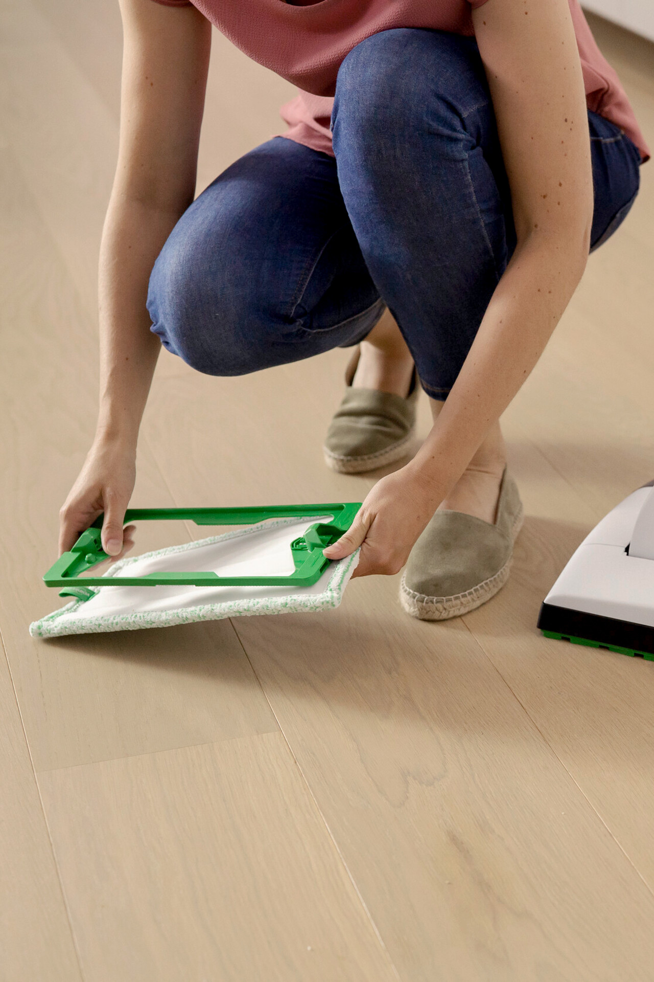 Person attaching a cleaning cloth to the Kobold VK7 for mopping a light wood floor.