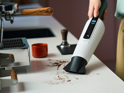 Frau saugt mit Kobold VK7 einen Hartboden im Haus-Eingangsbereich, während ein Mann sein Fahrrad zur Tür reinschiebt