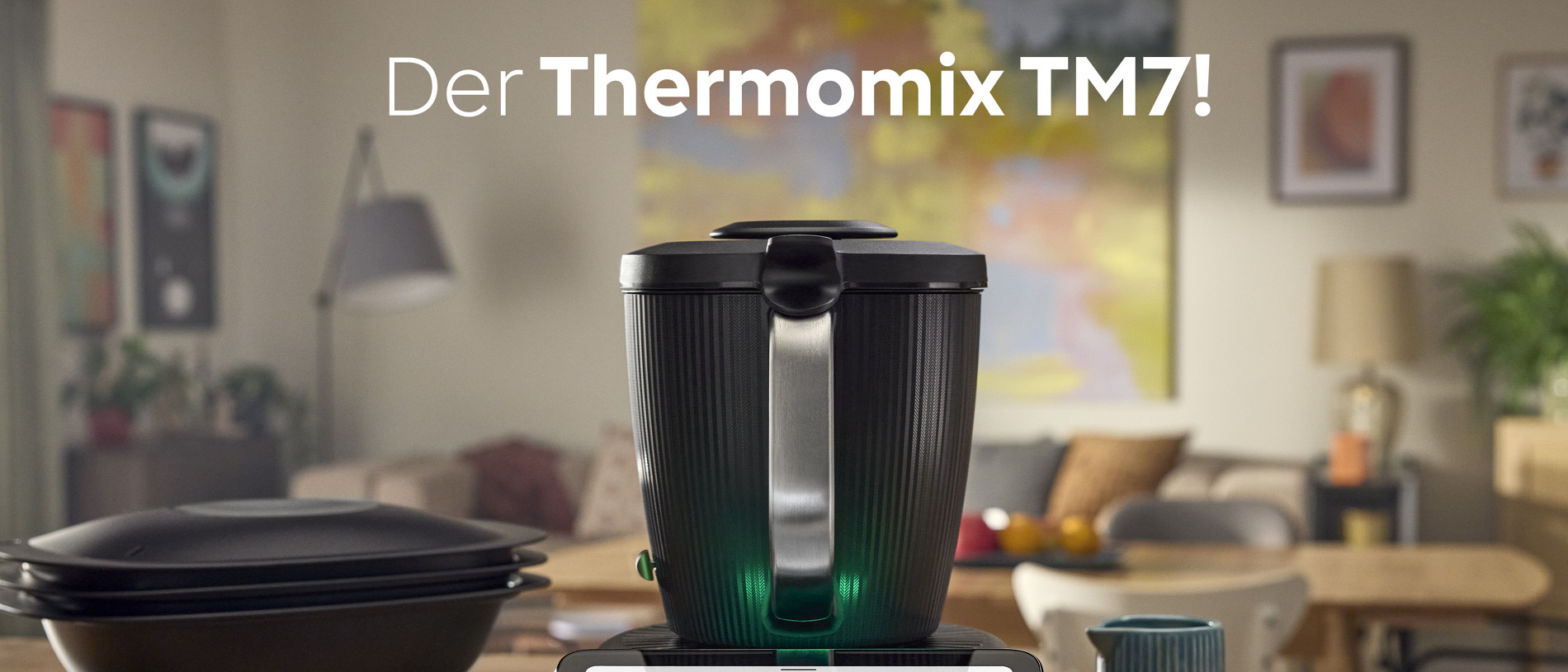 Thermomix® TM7 und Kochzutaten auf Küchenplatte, Wohnzimmer im Hintergrund