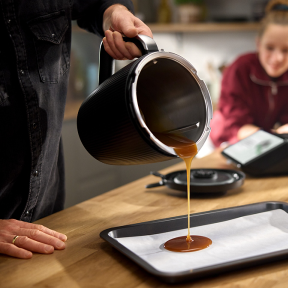 Taça do Bimby TM7 a verter caramelo para um tabuleiro com papel numa cozinha