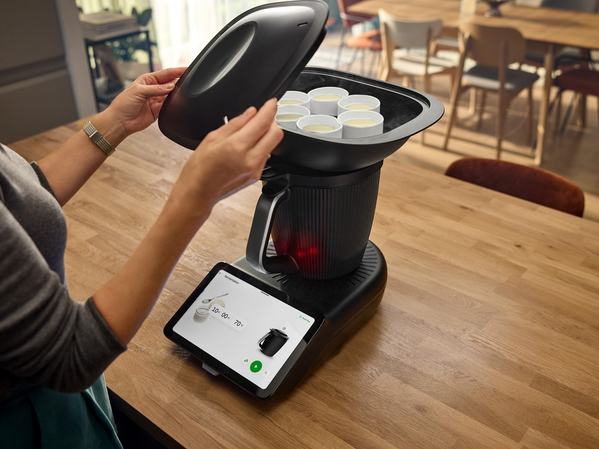 Person nutzt Thermomix® TM7 mit Varoma, der mit kleinen Schälchen befüllt ist, auf einem Holztisch.