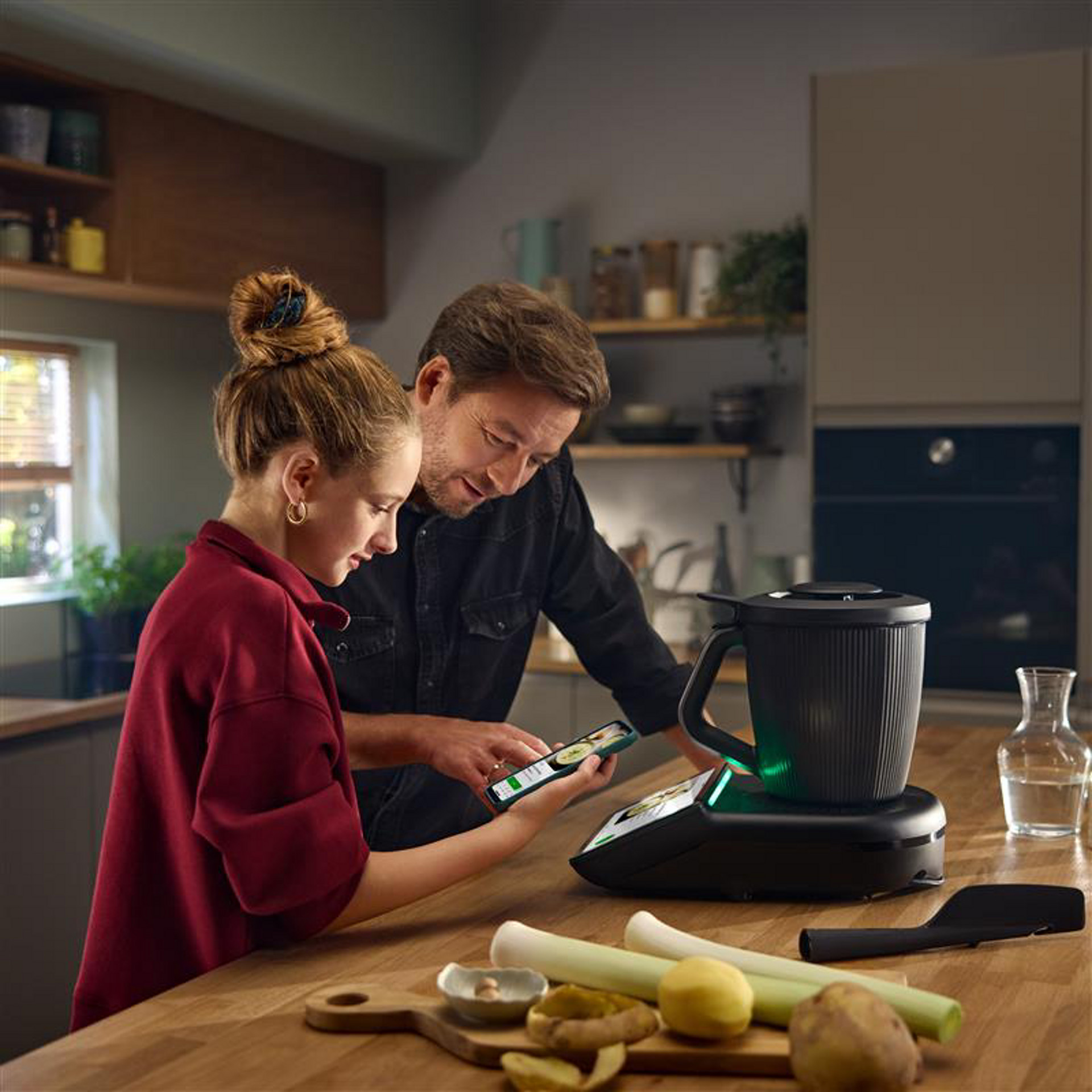 Two people cooking together using Thermomix® TM7 in a modern kitchen, with fresh ingredients on the counter.