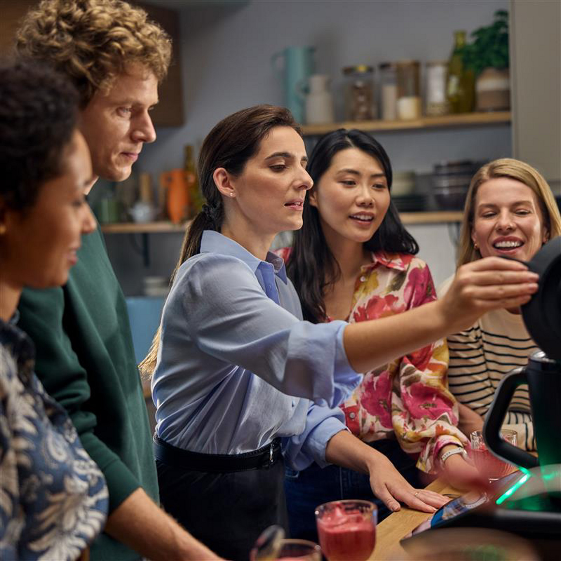 Group of people using a Thermomix® TM7 in a kitchen, preparing food or drinks together.