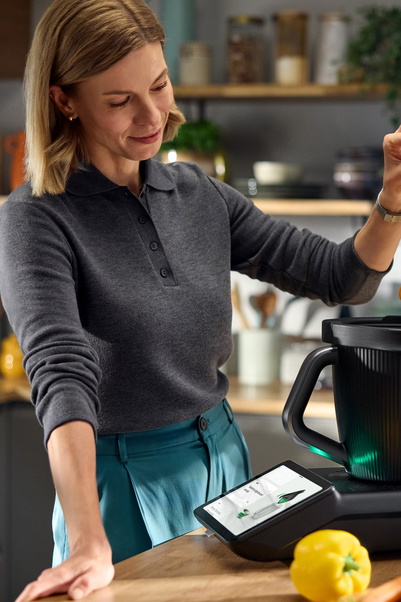 Woman preparing vegetable noodles using Thermomix® TM7 in a modern kitchen, surrounded by fresh ingredients.
