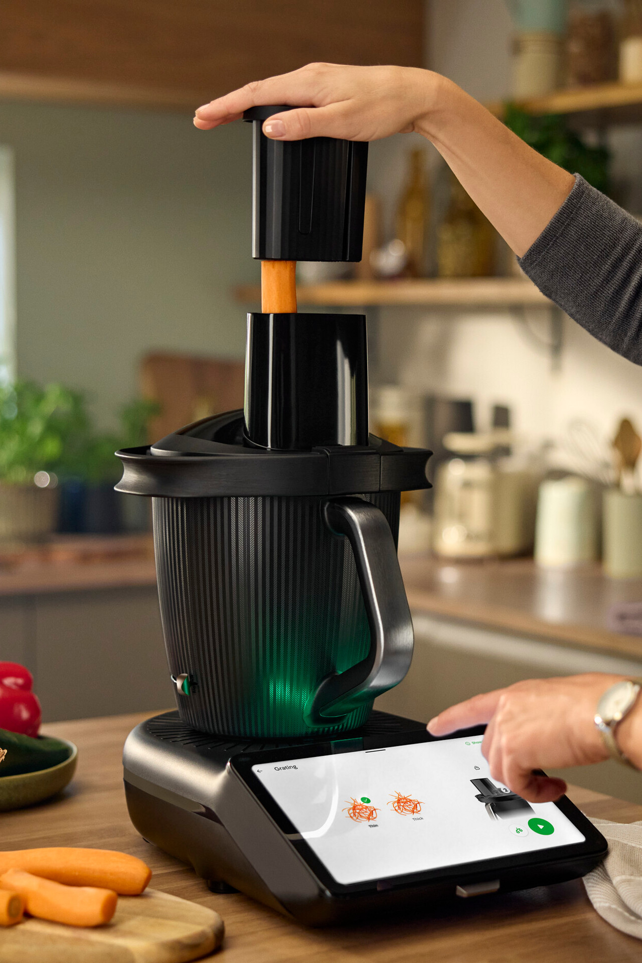 Kobieta używa Thermomix® TM7 z nakładką krojącą 2.0 Thermomix® TM7 ze spiralizerem do krojenia marchewek w nowoczesnej kuchni.