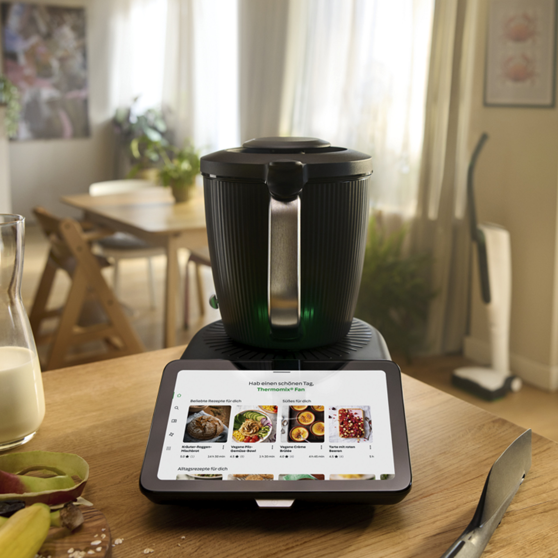 Thermomix® TM7 und Kobold VK7 stehen in einer hellen Küche, mit Lebensmitteln und Küchenutensilien auf dem Tisch.