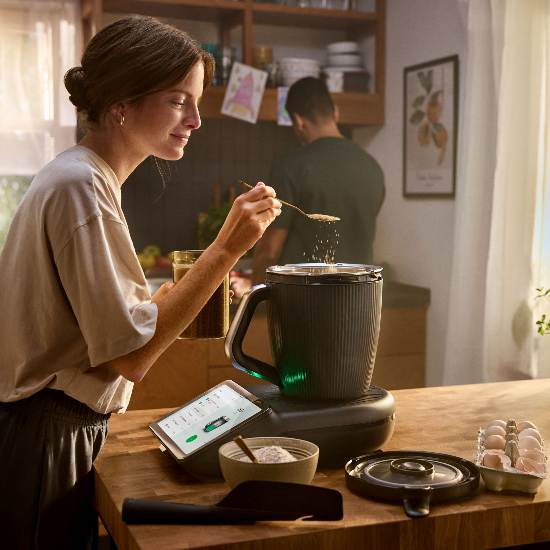 Woman preparing food using a Thermomix® TM7 on a kitchen counter with ingredients and utensils nearby.