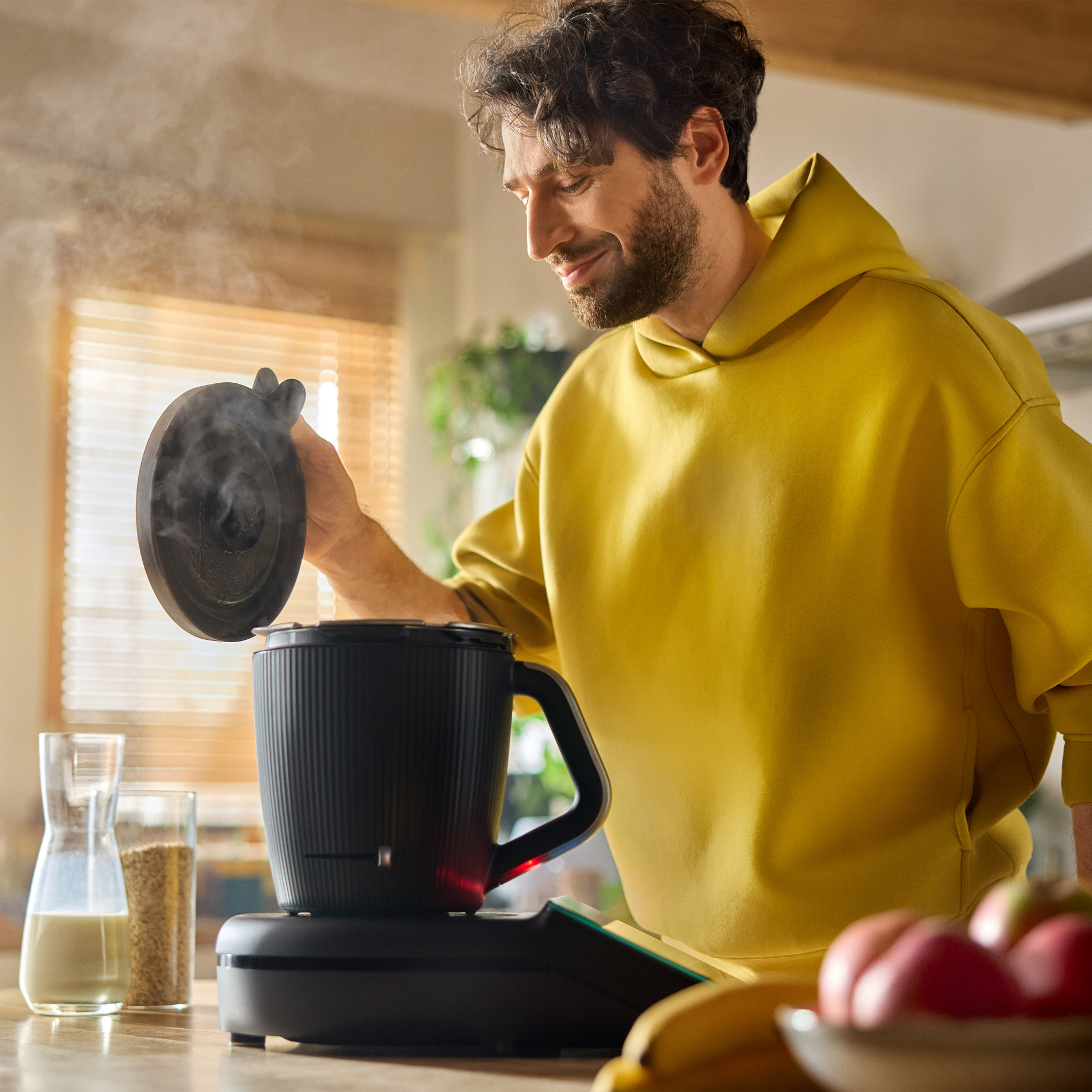 Person preparing food with a Thermomix® TM7 in a modern kitchen, lifting the lid with steam rising.