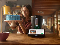 Frau präsentiert fertige Torte neben TM7 in der Küche