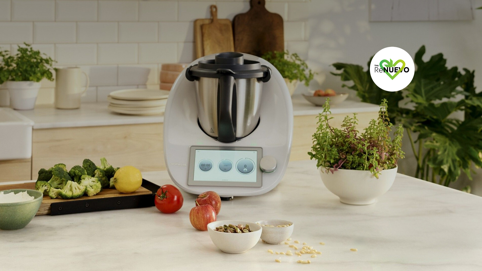 Thermomix® TM6 sobre una encimera de cocina rodeada de verduras, frutas, hierbas y utensilios.