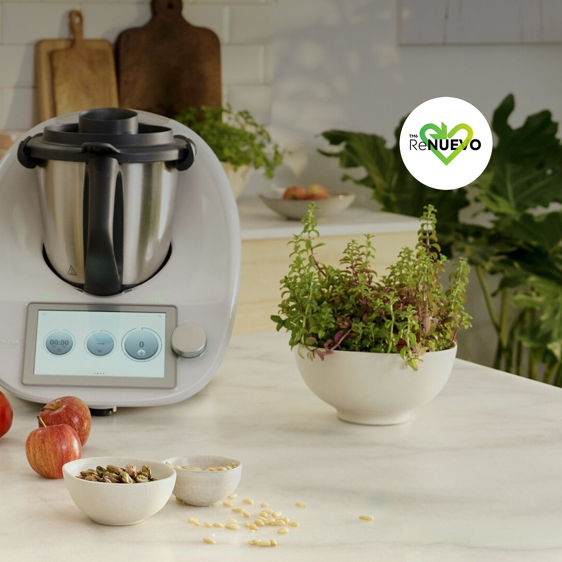 Thermomix® TM6 sobre una encimera de cocina rodeada de verduras, frutas, hierbas y utensilios.