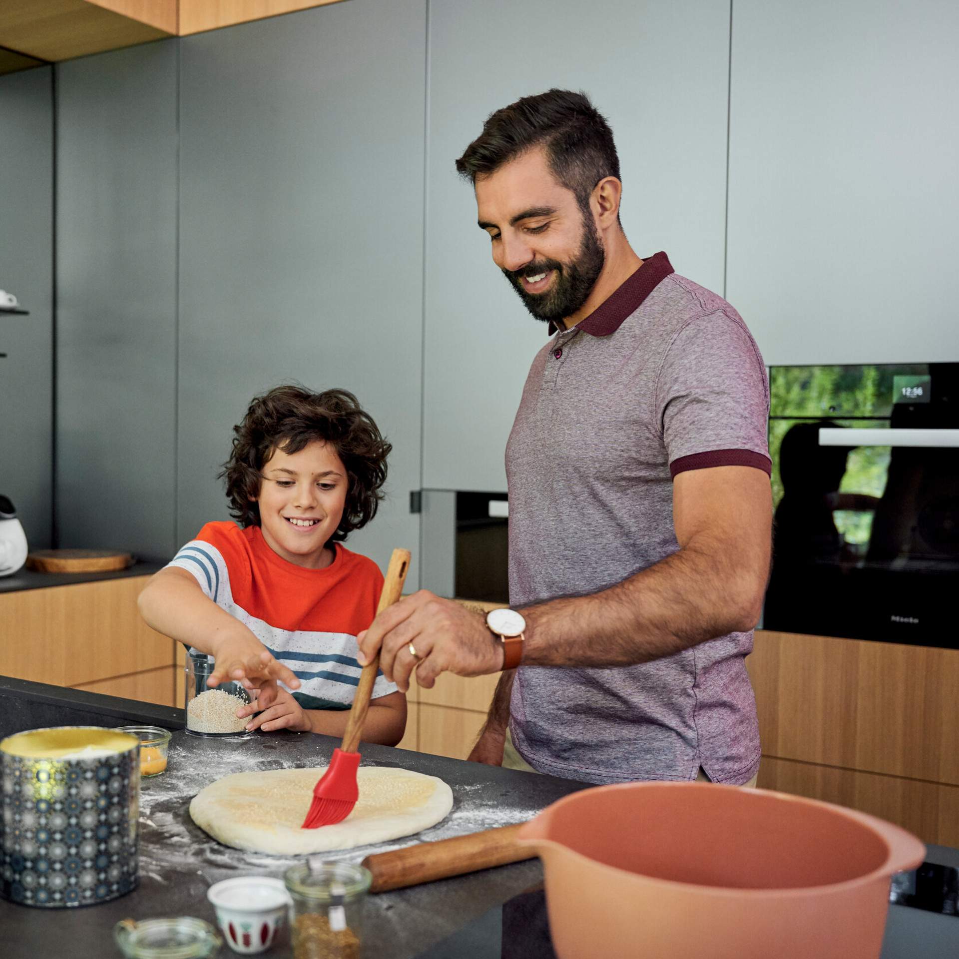 Adult and child prepare dough in a modern kitchen with Thermomix® TM6 visible on the counter.
