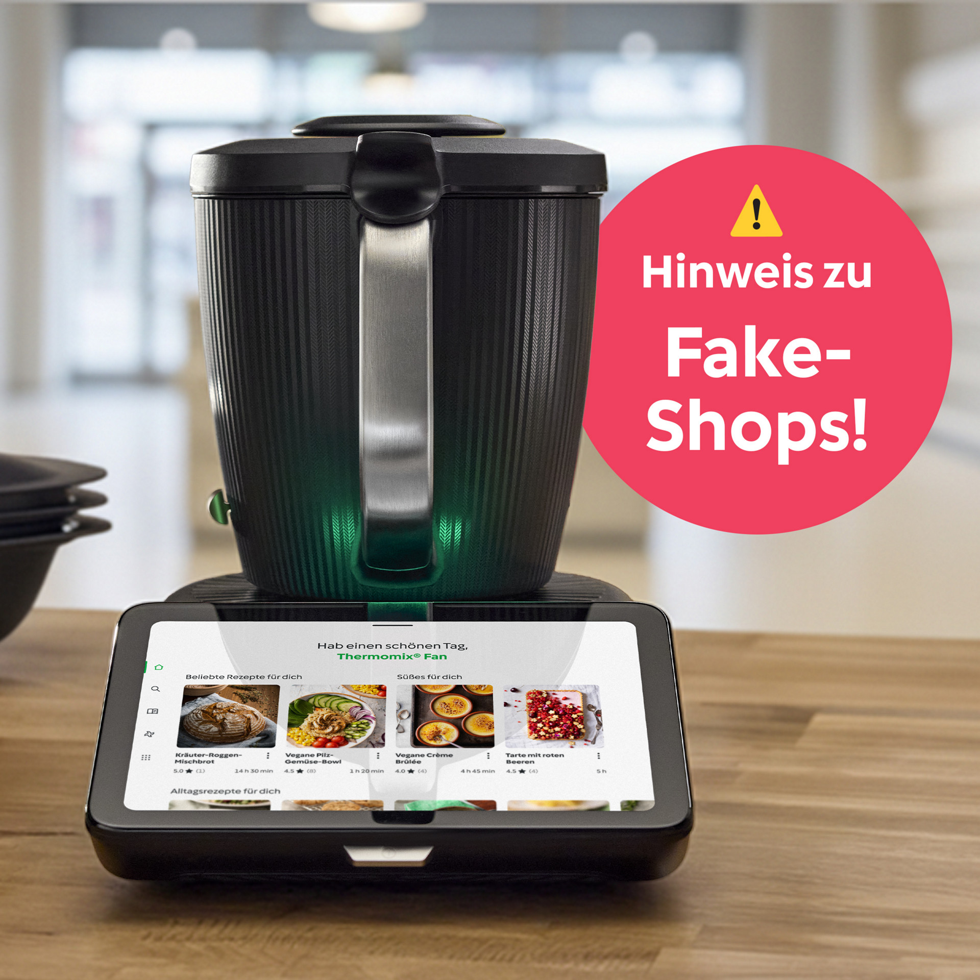 Thermomix® TM7 auf einer Küchenarbeitsplatte mit eingeschaltetem Display, Zubehör und rundem Hinweis zu Fake-Shops.
