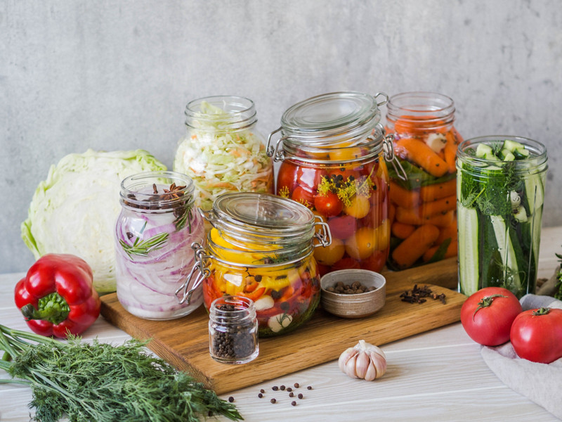 Cooking pickled vegetables. Salting various vegetables in glass jars for long-term storage. Preserves vegetables in glass jars. Variety fermented green vegetables on a wood board