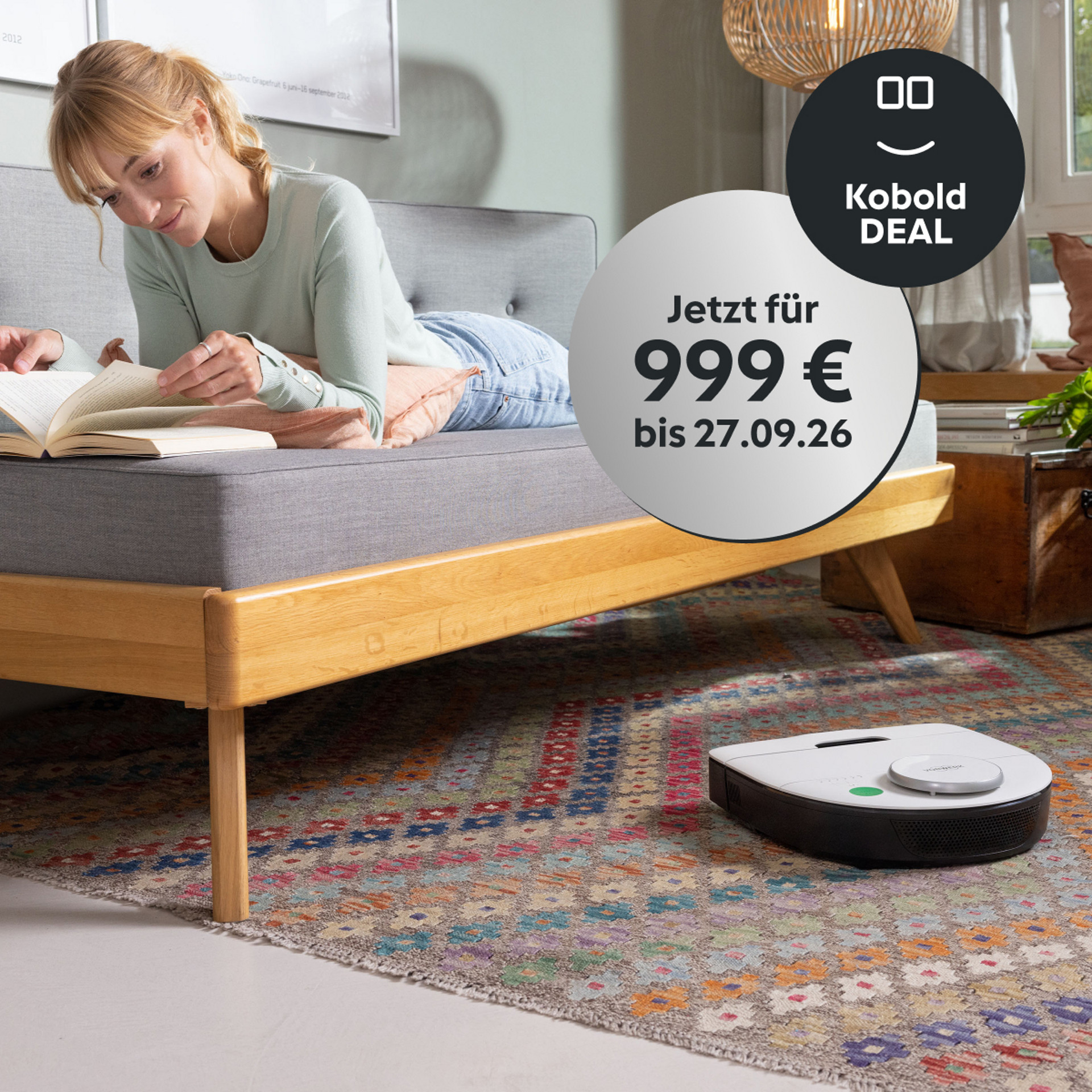 Frau liest auf einem Sofa, während der Kobold VR7 den Teppich reinigt; Aktionsbadge zeigt 999 € Kobold DEAL bis 27.09.26.