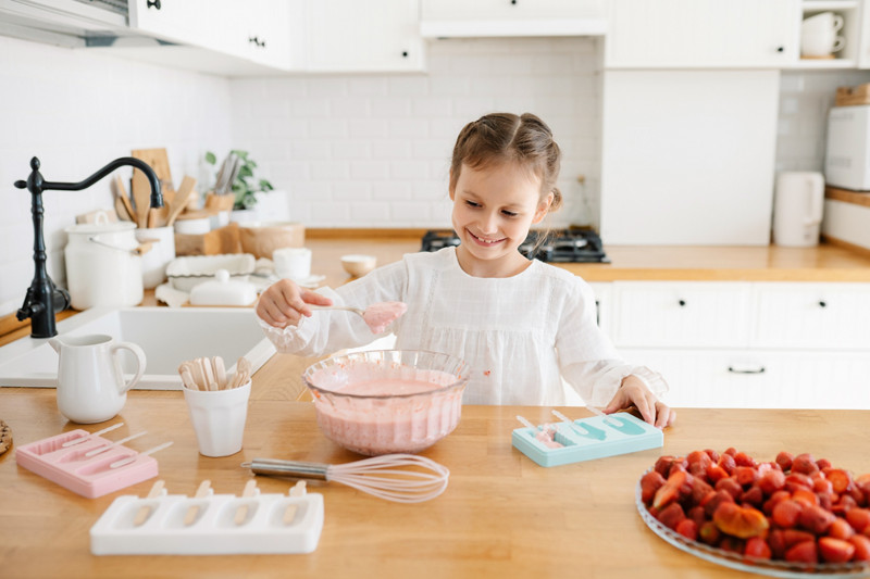 Cute little girl putting homemade strawberry ice cream in molds. Homemade ice cream.