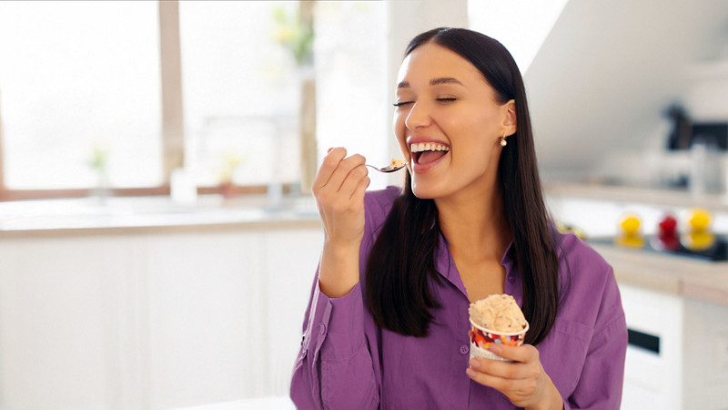 Attractive woman with tasty ice cream in kitchen, lady enjoy having cheat meal time and eating sweet dessert, space for text